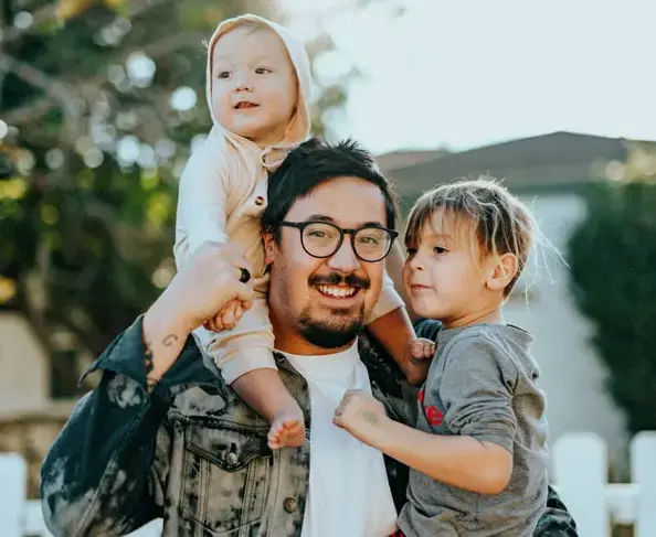 invōk.io petition & crowdfunding social platform - A man holding his two children in front of a white fence on invōk.io