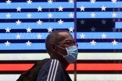 invōk.io petition & crowdfunding social platform - A man wearing a face mask walks past an American flag