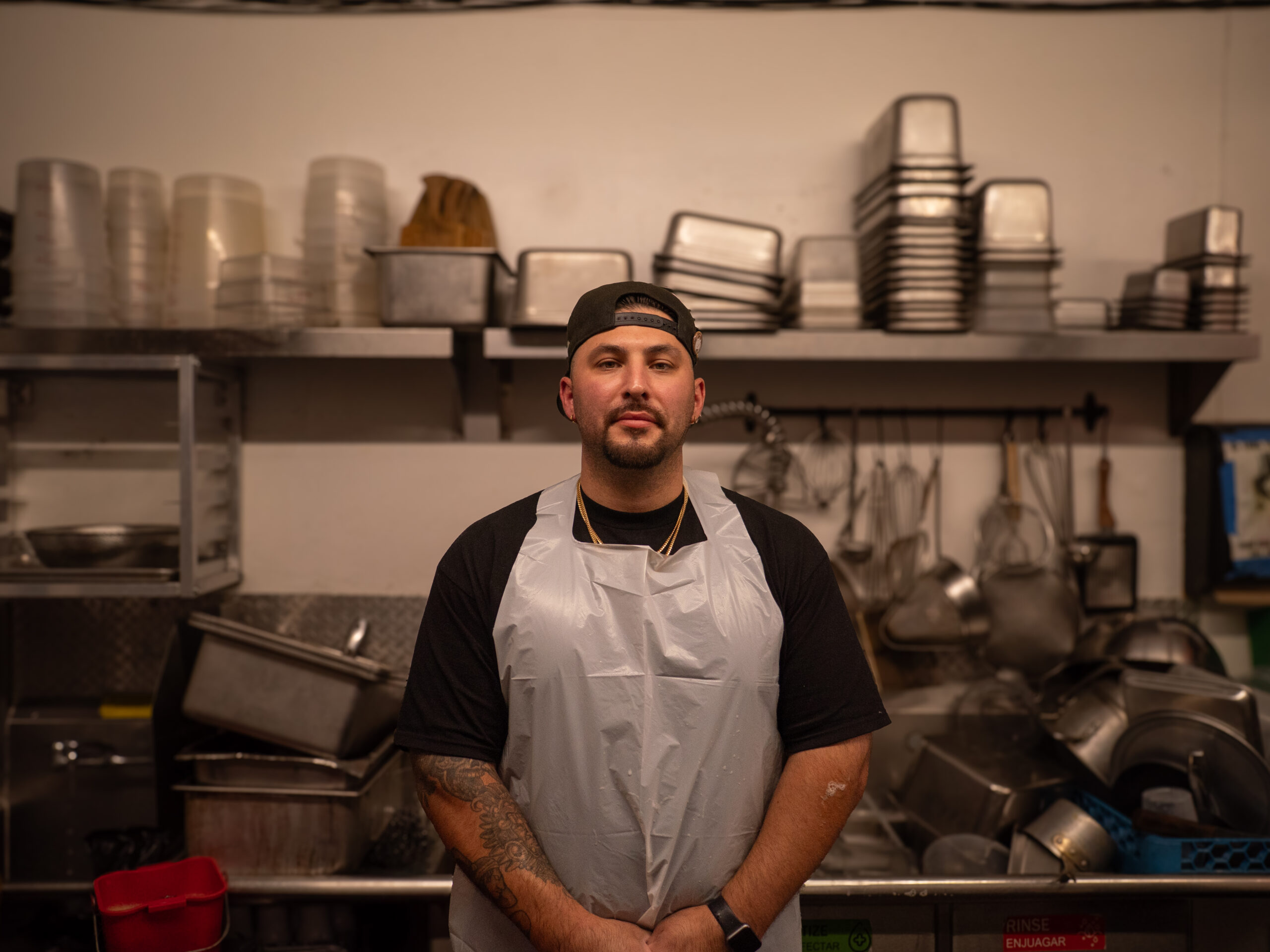These Nine L.A. Dishwashers Are the Real Heroes of Your Favorite Restaurants 2 a man in a cap wears an apron in front of a sink with many silver tubs and containers